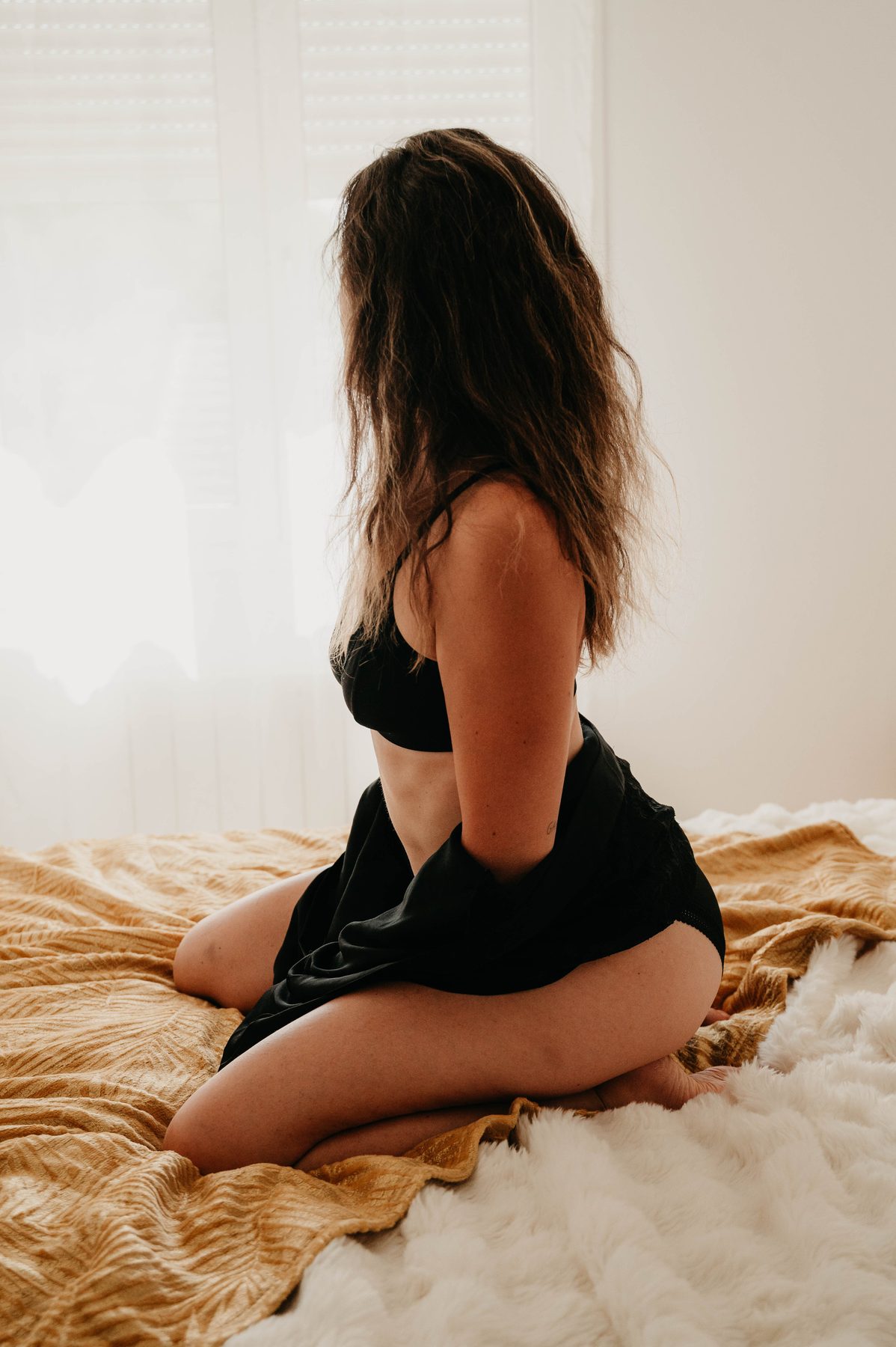 Femme assise sur le lit, à contre-jour devant la fenêtre