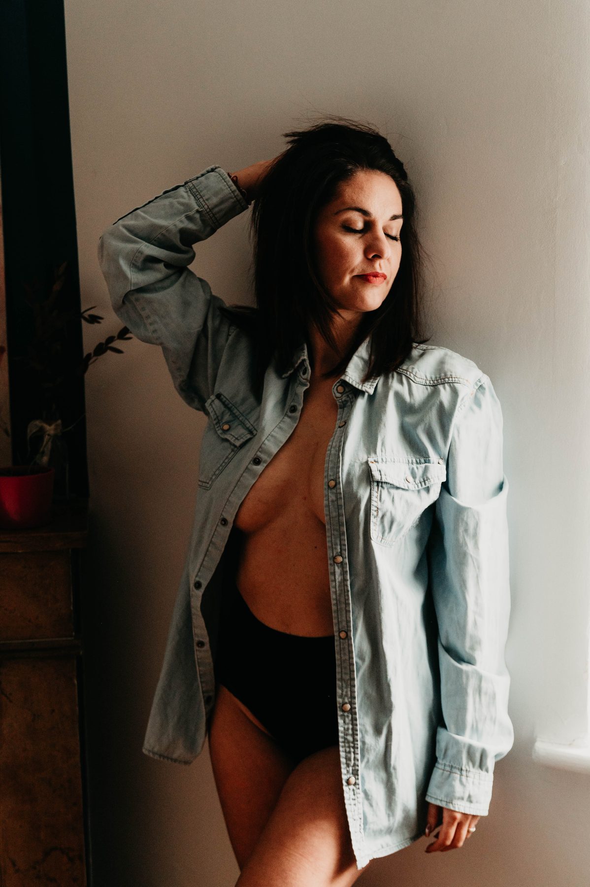 Chemise en jean ouverte près de la fenêtre, regard complice vers l’objectif